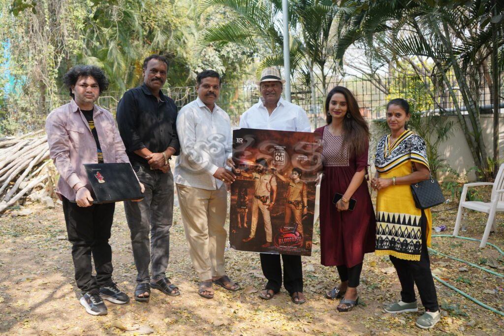 Group of six individuals posing together, holding a movie poster outdoors in a natural setting.